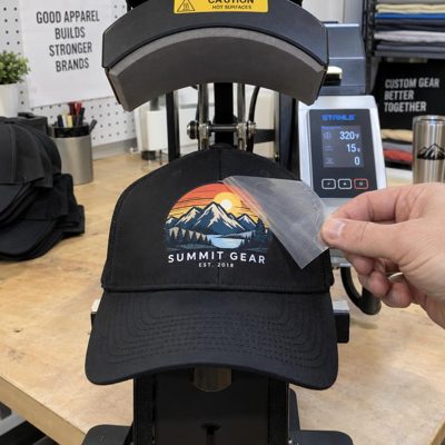 A DTF transfer being peeled off a cap on a cap heat press